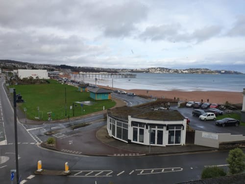The Sands Hotel beachfront view with pier, sandy beach, coastal town, and cloudy sky in Paignton