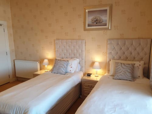 Twin bedroom at The Sands Hotel Paignton with beige quilted headboards, bedside lamps, and patterned wallpaper