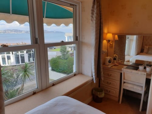 The Sands Hotel bedroom in Paignton with bay views, wooden furniture, and seaside landscape visible through balcony doors