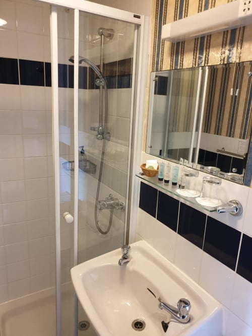 Modern bathroom at The Sands Hotel Paignton with glass shower enclosure, white sink, and striped wallpaper