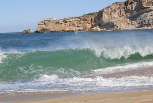 grosse vague devant la falaise sur la plage de Nazaré