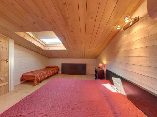 Chambre mansardée avec plafond en bois, puits de lumière, deux lits aux courtepointes rouges et lumière naturelle à la villa Le Maquis Plage