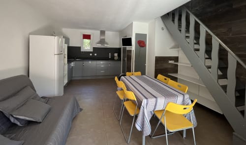 Cuisine ouverte donnant sur la salle à manger de la villa Le Maquis Plage, avec chaises jaunes, équipements modernes et escalier