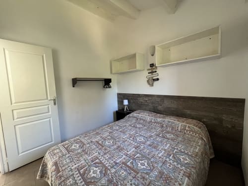 Chambre de la villa Le Maquis Plage à Poggio-Mezzana avec lit queen-size, tête de lit en bois foncé, rangements muraux et porte blanche