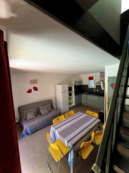Intérieur de villa à Le Maquis Plage avec table à manger, chaises jaunes, cuisine, canapé et chambre à Poggio-Mezzana
