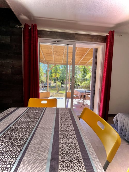Salle à manger lumineuse avec chaises jaunes, chemin de table motifs, portes vitrées ouvertes sur la terrasse de la villa Le Maquis Plage
