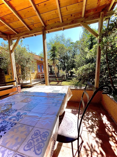 Terrasse ombragée avec carrelage bleu à motifs à la villa Le Maquis Plage à Poggio-Mezzana, vue sur le jardin