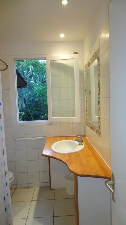 Salle de bain moderne de la villa Le Maquis Plage avec vasque en bois, douche et fenêtre sur le jardin