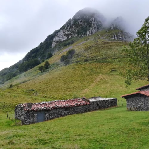 Tradicional caserío de piedra con tejado de barro ubicado en verde pradera bajo la cumbre brumosa de la montaña en Gipuzkoa, España