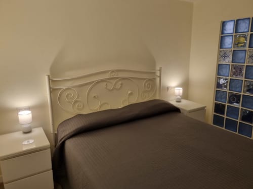 Comfortable bedroom with decorative wrought iron headboard, dark bedding, side lamps, and decorative window panel in B&B Il