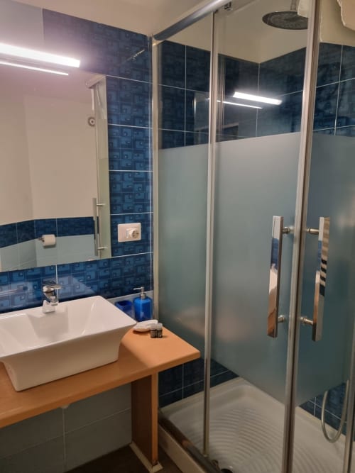Modern bathroom in B&B Il Conservatorio Naples suite with blue tile accents, white sink, glass shower enclosure and wooden