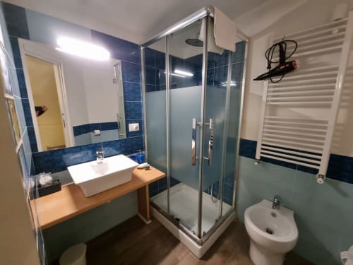 Modern bathroom in B&B Il Conservatorio Naples with blue tiled walls, glass shower enclosure, white vessel sink, and heated