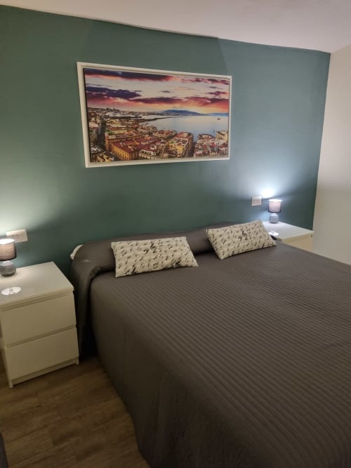 Modern bedroom at B&B Il Conservatorio Naples with sage green accent wall, dark bed, cream pillows, white nightstands, and