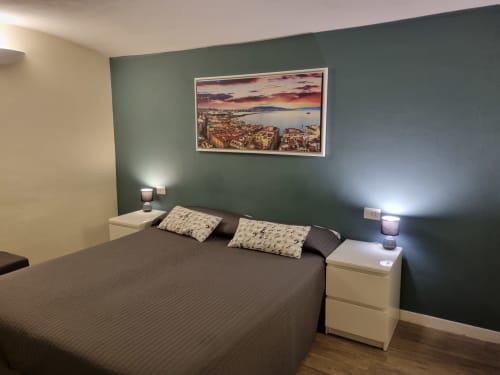 Modern bedroom in Naples B&B with green accent wall, double bed, white nightstands, and sunset coastal artwork above