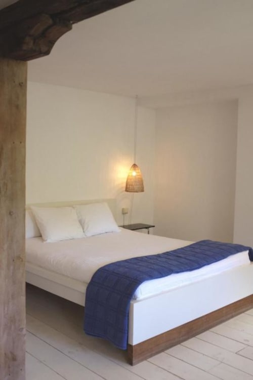 Dormitorio moderno en Casa rural MAÑARINEGI de Gipuzkoa con cama blanca, camino azul marino, luz colgante y detalles de vigas de madera