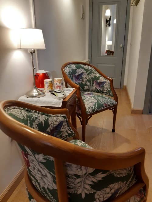 Cozy seating area at Casa Rural La Perla with upholstered wooden chairs, floral fabric, lamp, and entrance door in