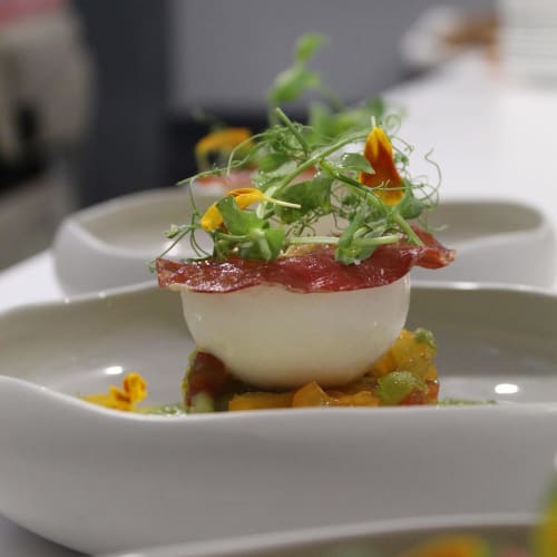 Plat élégamment dressé au Pavillon Des Millesimes avec centre onctueux, charcuterie, microherbes et fleurs comestibles