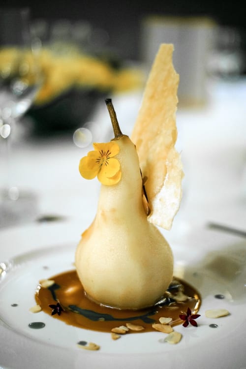 Artistic poached pear dessert with yellow flower and crispy wafer, plated at Pavillon Des Millesimes SPA