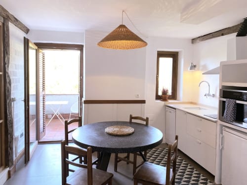 Luminosa zona de cocina-comedor en apartamento Casa rural MAÑARINEGI con mesa redonda negra, sillas de madera, lámpara colgante tejida y