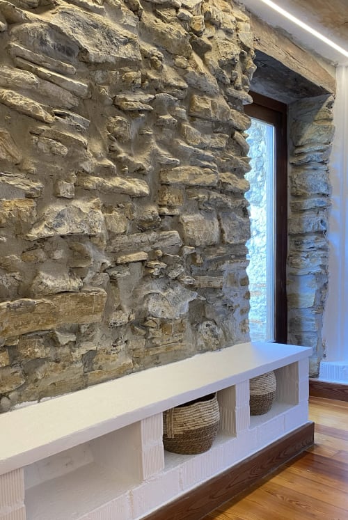 Pared de piedra rústica con estante de madera y cestas tejidas en apartamento rural de Gipuzkoa con vista al jardín