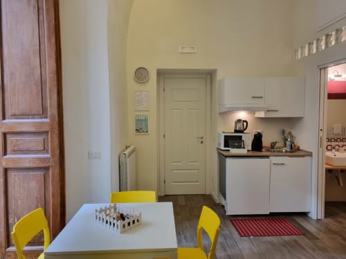 Modern kitchenette with white cabinetry, yellow chairs, and dining table in Suite de luxe at B&B Il Conservatorio Naples