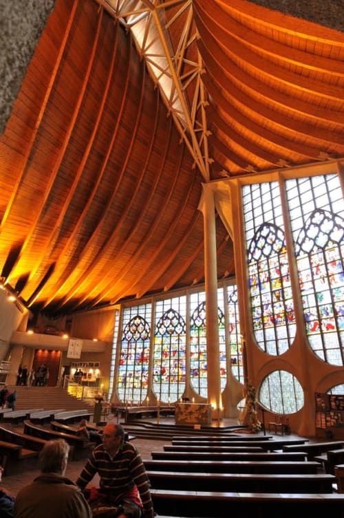 Interior de capilla moderna en Hotel Dandy Rouen con techo de madera, vidrieras de colores y bancos.