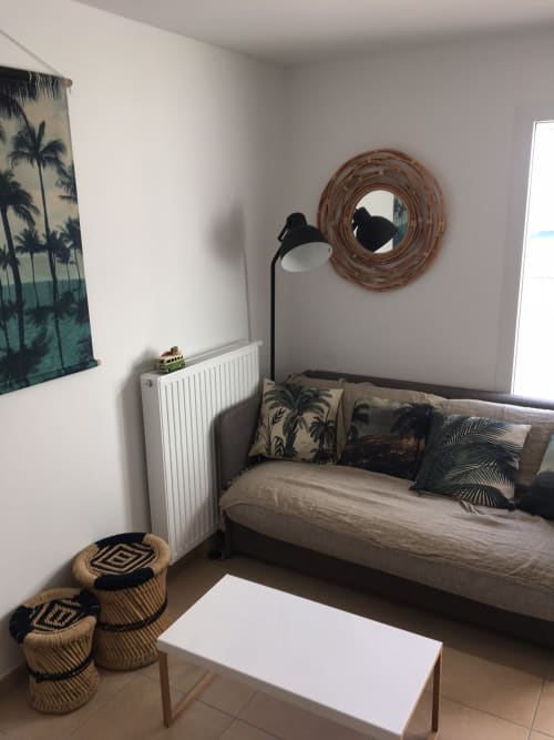Tropical-themed bedroom at Cote Et Dune hotel with palm tree decor, woven mirror, and comfortable daybed seating