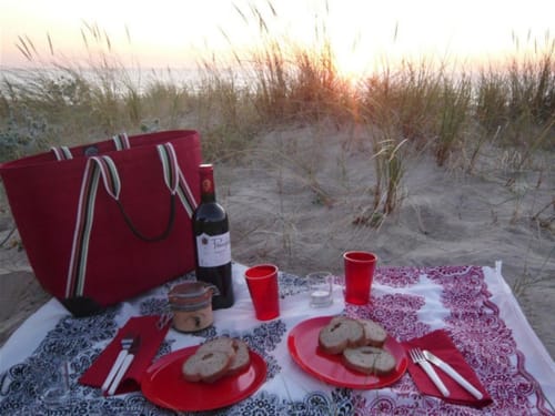 Romantic beach picnic setup at Cote Et Dune with wine, bread, and red accents at sunset in Biscarrosse