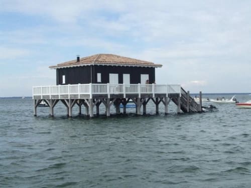 Pavillon en bord de mer Côte Et Dune sur pilotis à Biscarrosse Plage, avec balustrades blanches et toiture carrelée surplombant l'eau