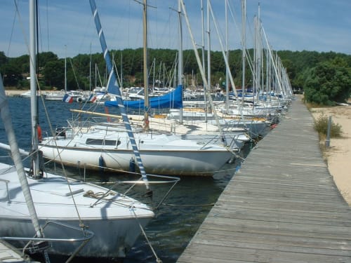 Rangée de voiliers amarrés à la marina de Biscarrosse Plage avec débarcadère en bois et forêt en arrière-plan