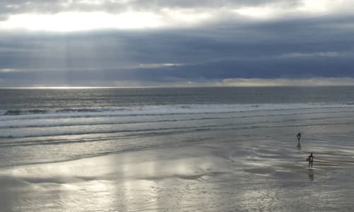 Des surfeurs entrant dans l'océan à la plage de Biscarrosse sous un ciel nuageux dramatique