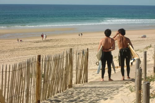 Deux surfeurs se dirigeant vers la plage à Côte Et Dune, Biscarrosse Plage, avec un chemin d'accès en bois et vagues océanes