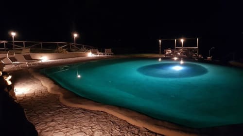 Piscina illuminata di notte con acqua turchese, lettini e vista sul mare a Casale di Poggioferro, Toscana