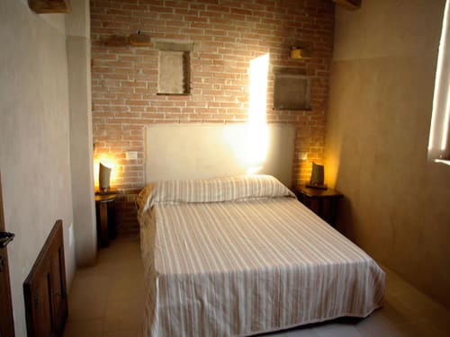 Camera accogliente al Casale di Poggioferro con letto a righe, muro in laterizio a vista, illuminazione calda e arredamento rustico a Poggioferro