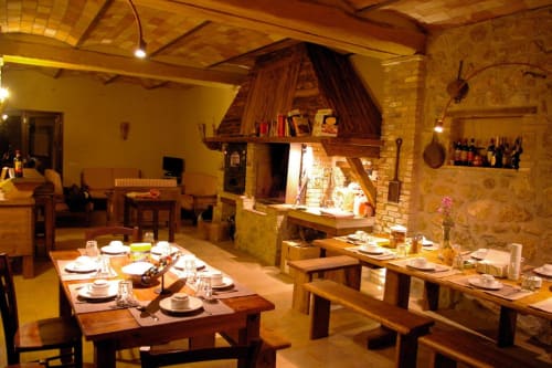 Sala da pranzo rustica al Casale di Poggioferro con tavoli in legno, camino e illuminazione calda in Toscana