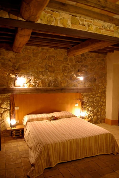 Camera rustica in pietra al Casale di Poggioferro B&B con travi in legno, illuminazione calda e biancheria a righe
