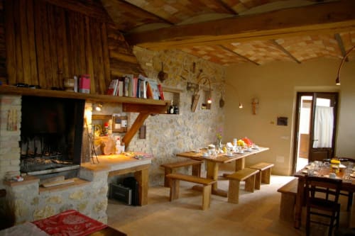 Zona pranzo rustica con camino presso il Casale di Poggioferro B&B in Toscana, con tavoli in legno e focolare in pietra
