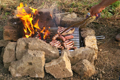 Cucina all'aperto intorno al fuoco a Casale di Poggioferro con carni grigliate sul focolare in pietra
