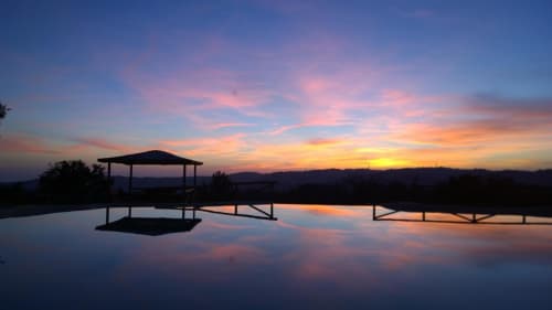 Tramonto a Casale di Poggioferro con padiglioni in silhouette riflessi nell'acqua ferma, Toscana