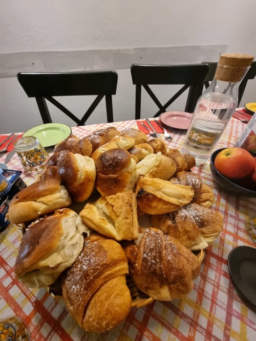 Desayuno en B&B Il Conservatorio en Nápoles con pasteles variados, croissants, frutas frescas y agua sobre mantel a cuadros
