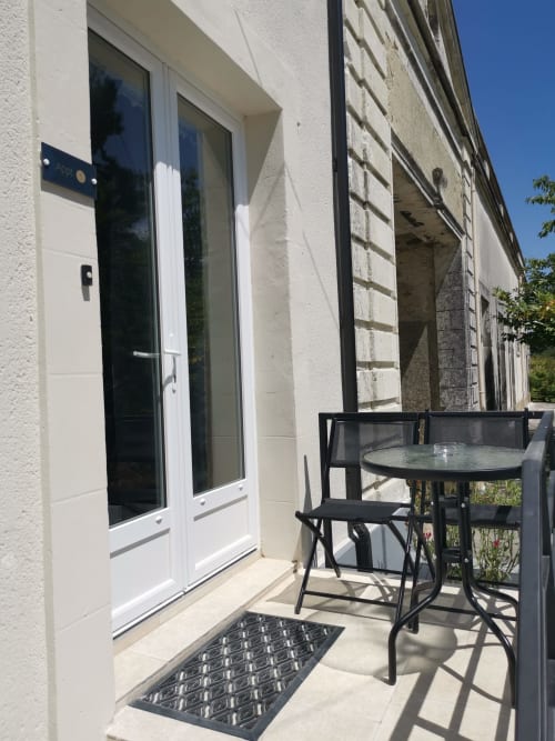 Terrasse extérieure de la Résidence L'Hermitière avec table noire, chaises et portes vitrées menant à l'entrée de l'appartement en Loire
