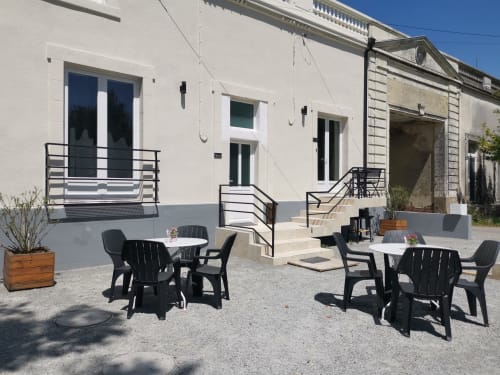 Terrasse extérieure de la Résidence L'Hermitière avec chaises Adirondack noires, bâtiments blancs et vue sur le jardin
