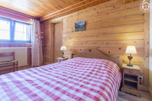 Chambre douillette en bois du Chalet La Louvière avec literie à carreaux roses, vue montagne et éclairage chaleureux