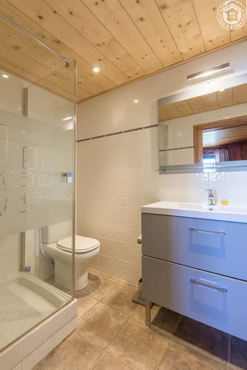 Salle de bain moderne du Gîte de la Louvière avec douche vitrée, meuble vasque bleu et plafond en bois
