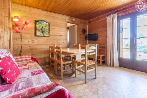 Intérieur chaleureux du Chalet La Louvière avec salle à manger, télévision, vue sur les montagnes et literie à carreaux rouges