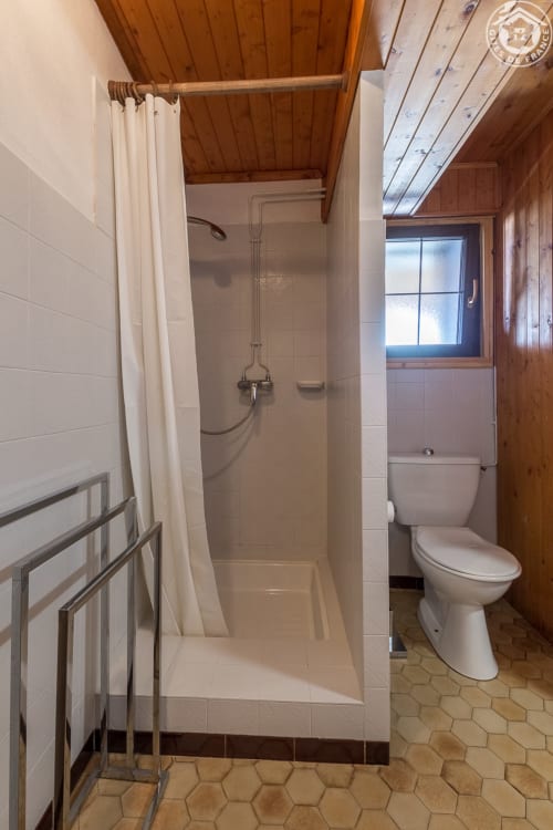 Spacieuse salle de bains avec douche et toilettes, plafond en bois et carrelage hexagonal au Chalet La Louvière