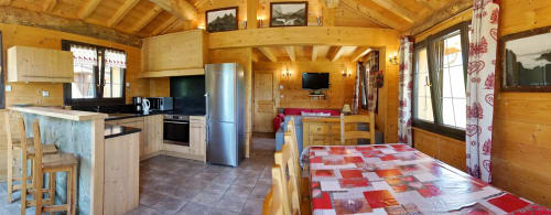 Cuisine et salle à manger du chalet La Louvière avec poutres en bois, nappe à carreaux rouges et vue sur les montagnes