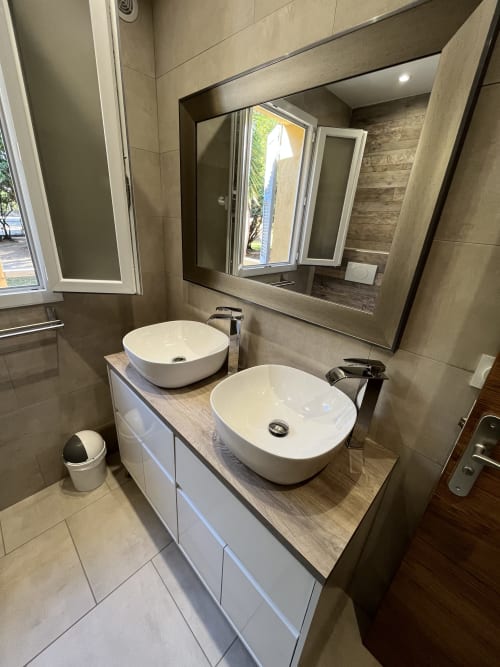 Salle de bain moderne de la villa Le Maquis Plage avec doubles vasques blanches, miroir à cadre sombre et finitions carrelage neutre