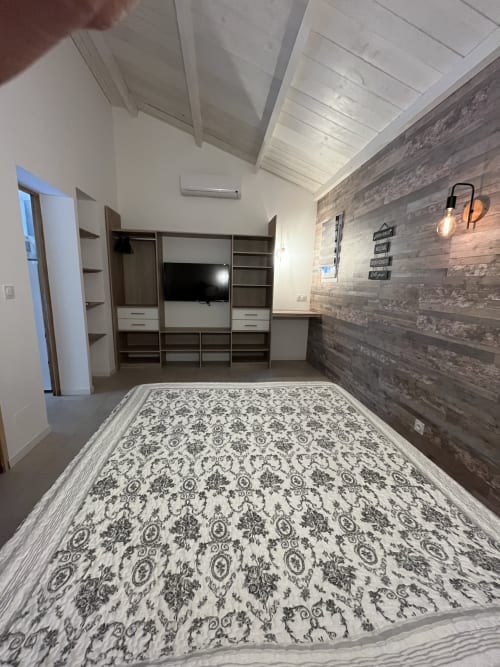 Spacieuse chambre principale de la villa Le Maquis Plage avec lit à motifs, meuble de divertissement moderne, mur d'accent en bois