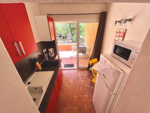 Cuisine moderne de la villa Le Maquis Plage à Poggio-Mezzana, armoires rouges, appareils inox, vue sur la terrasse